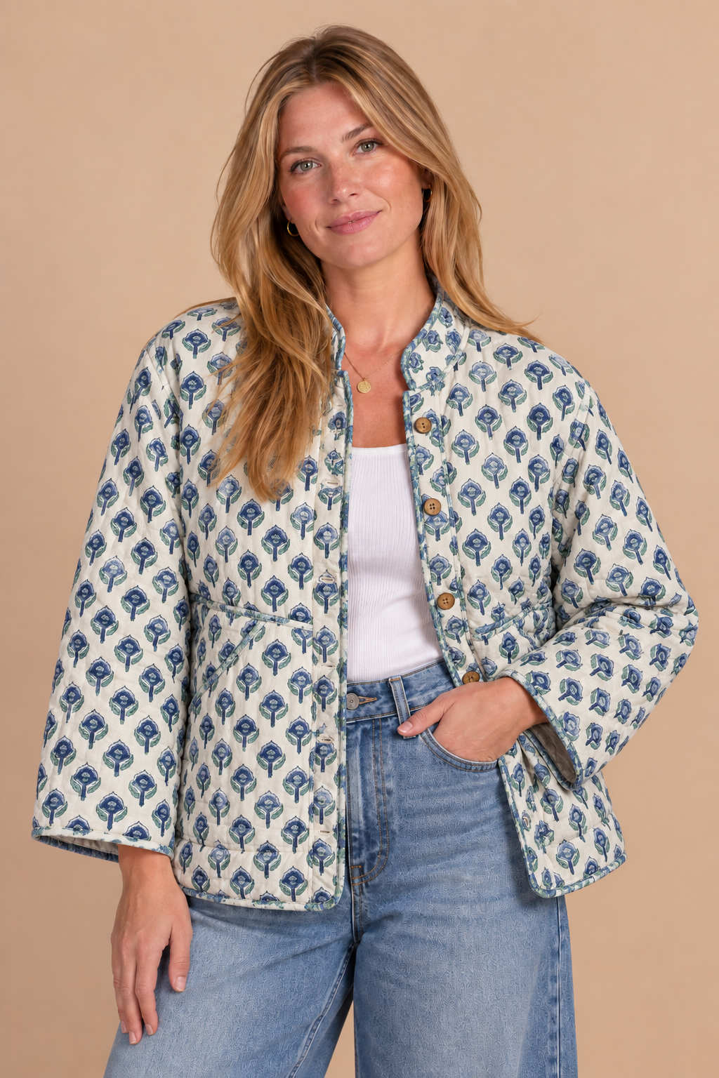 A woman modeling a cropped, long-sleeve jacket with a blue and white geometric block-print pattern, styled with a white tank top and light-wash blue jeans against a solid beige background.
