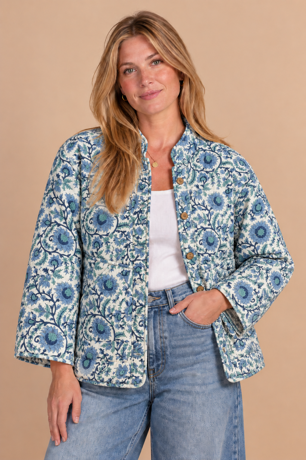 A woman modeling a blue and white floral patterned jacket over a white top and blue jeans, standing against a solid beige background.