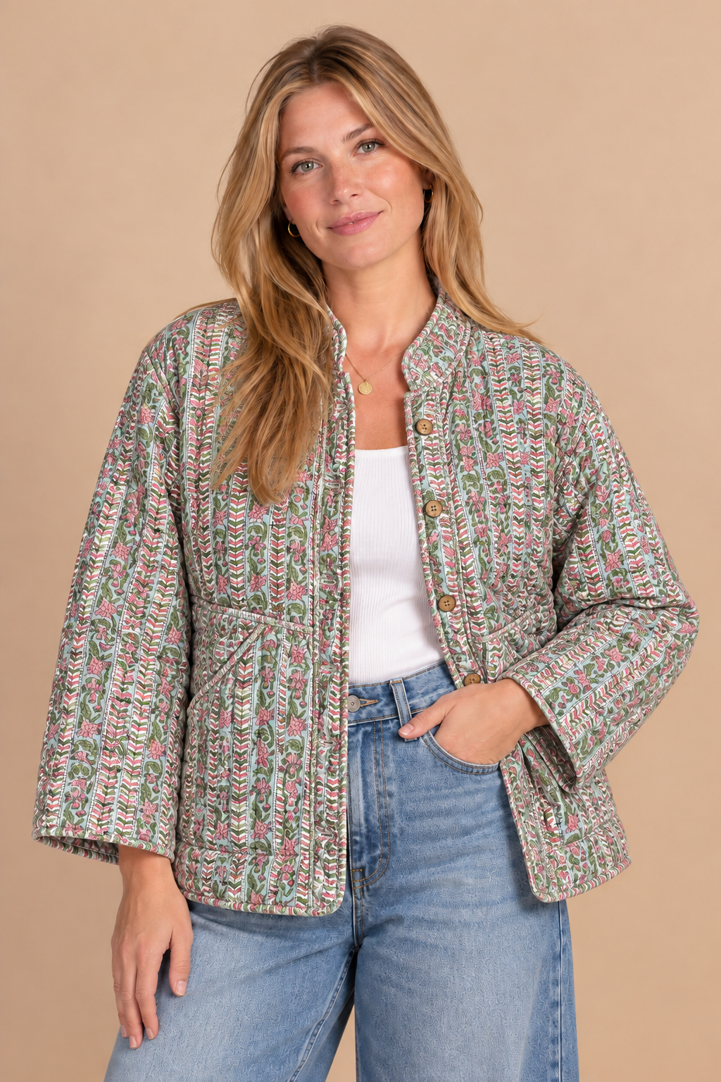 A woman modeling a cropped, long-sleeve tweed jacket with a multicolor pattern of pink, green, and blue on a beige base, worn over a white tank top and blue jeans against a solid beige background.