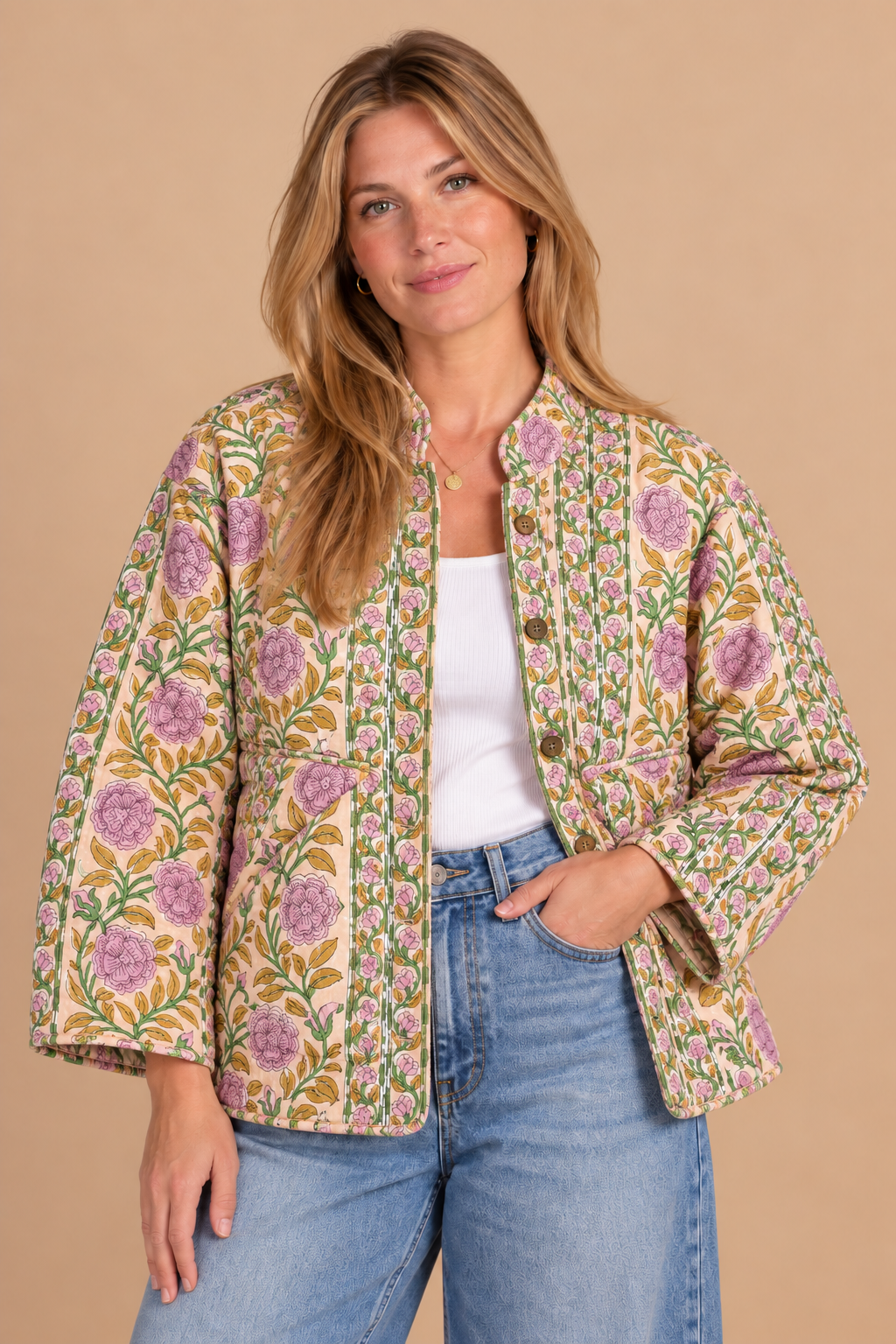 A woman wearing a beige button-front jacket with a colorful floral print in purple, green, and yellow, styled with a white tank top and blue jeans against a solid beige background.