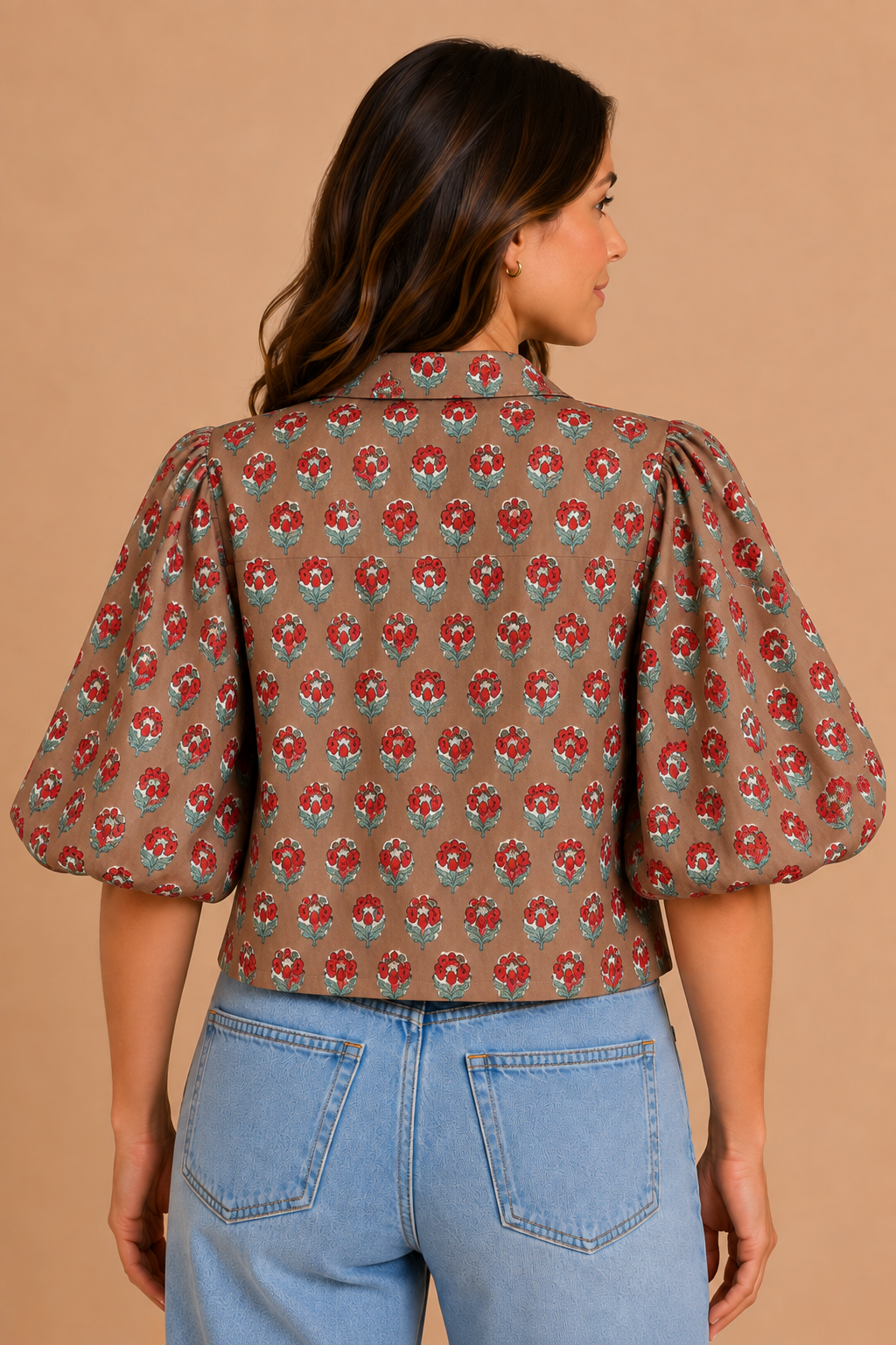 A woman shown from the back wearing a brown puff-sleeve blouse with a red and teal floral pattern, paired with light blue jeans, against a solid tan background.
