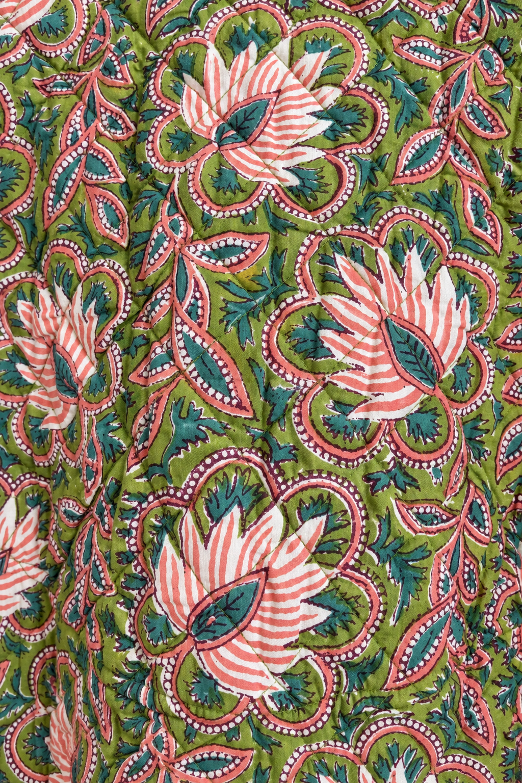 A close-up of a quilted fabric featuring a vibrant floral and paisley block print. The pattern consists of coral-pink and white striped flowers, deep teal leaves, and red-bordered paisley motifs over an olive green background.