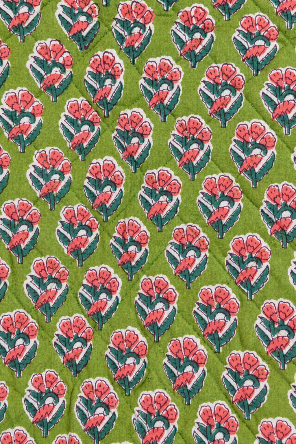 A close-up of a quilted fabric featuring a repeating block-print style floral pattern in pink, white, and dark green on a lime green background.