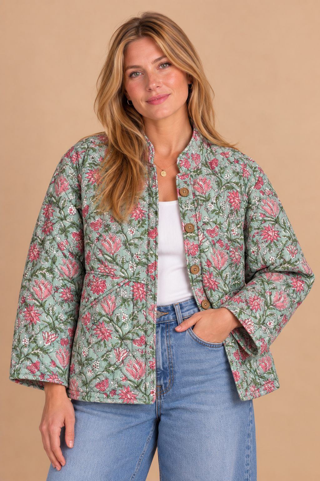 A woman wearing a light sage green cropped jacket with a pink and green floral pattern, styled over a white top and blue jeans, against a solid beige background.