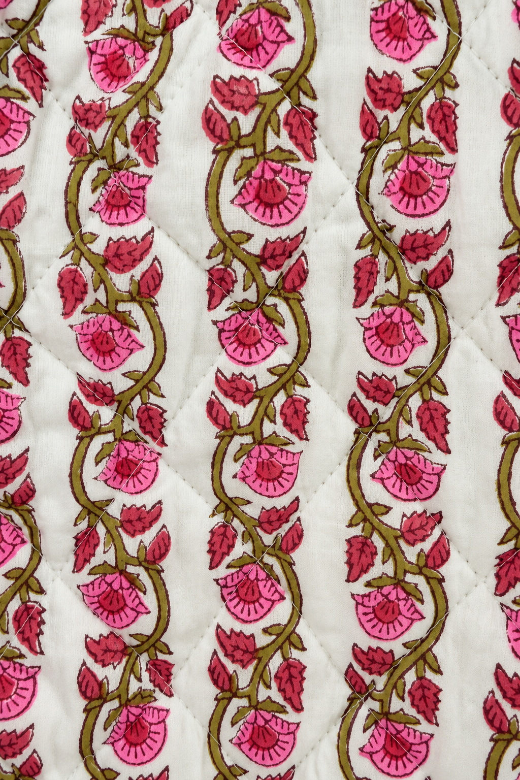 A close-up of a quilted fabric featuring a repeating vertical pattern of pink flowers and green vines on a white background.