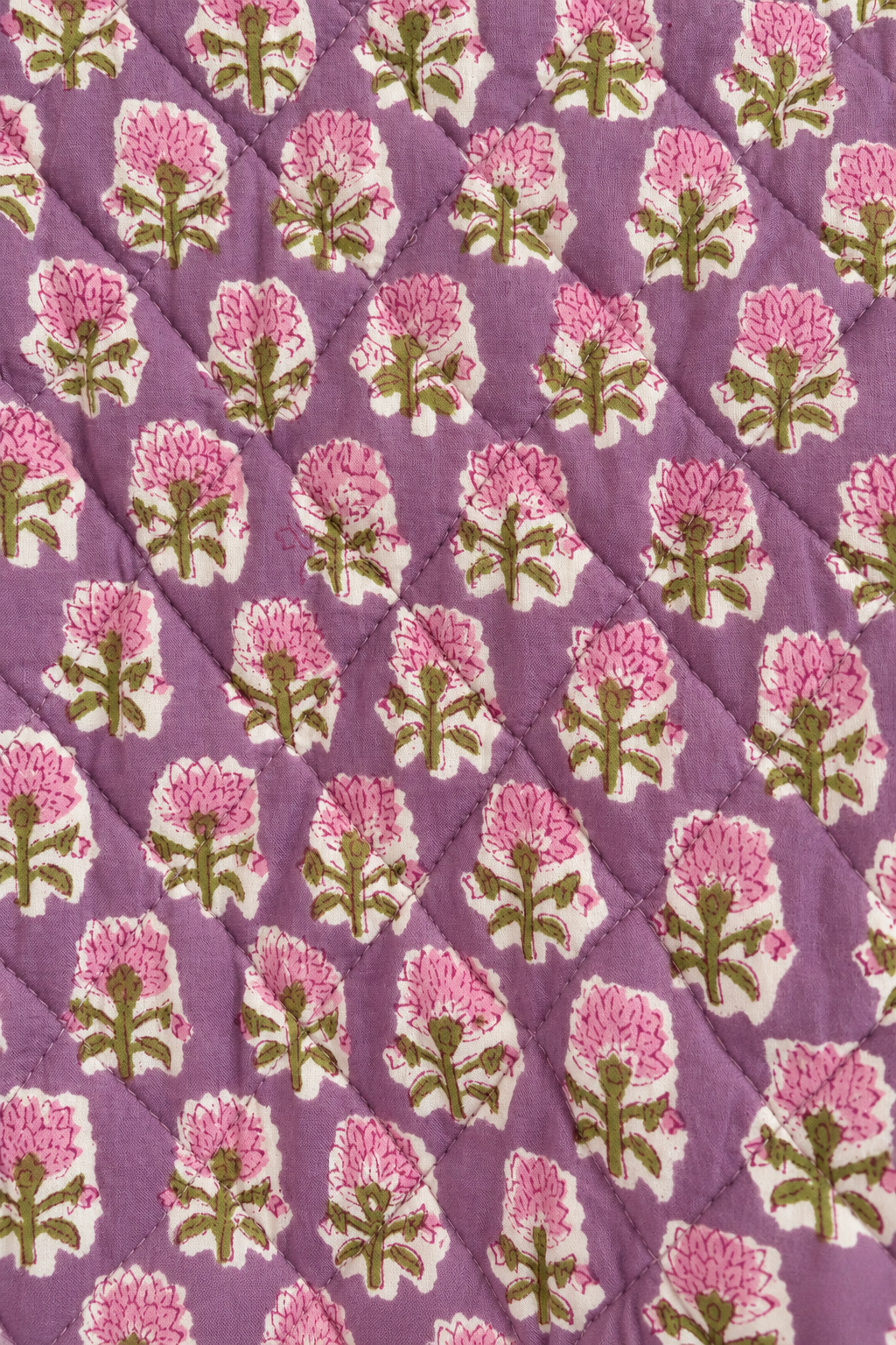 A close-up of a quilted fabric featuring a repeating block print of pink flowers with green stems on a dusty purple background.