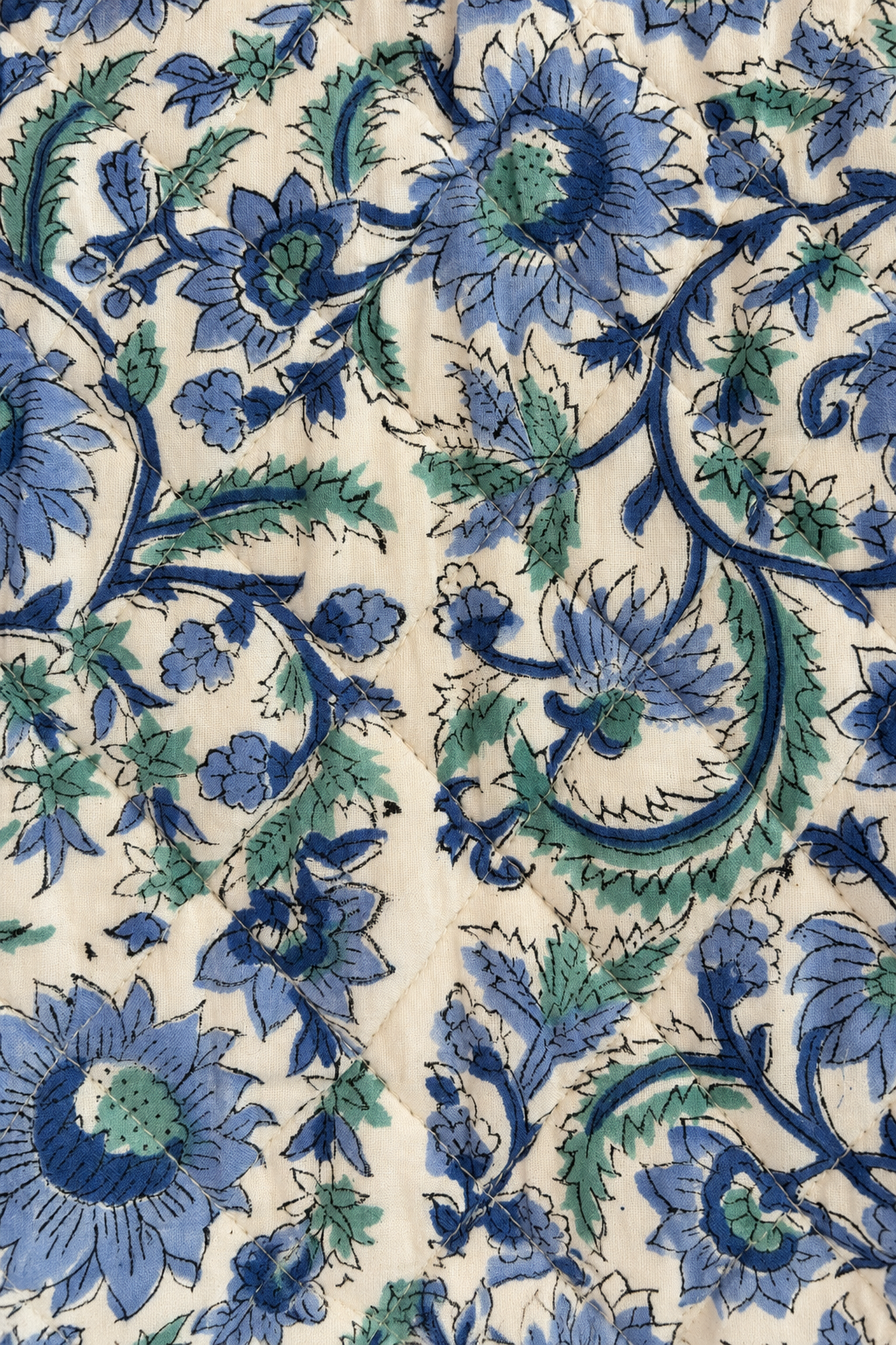 A close-up of a cream-colored fabric with a detailed blue and green floral block print pattern.