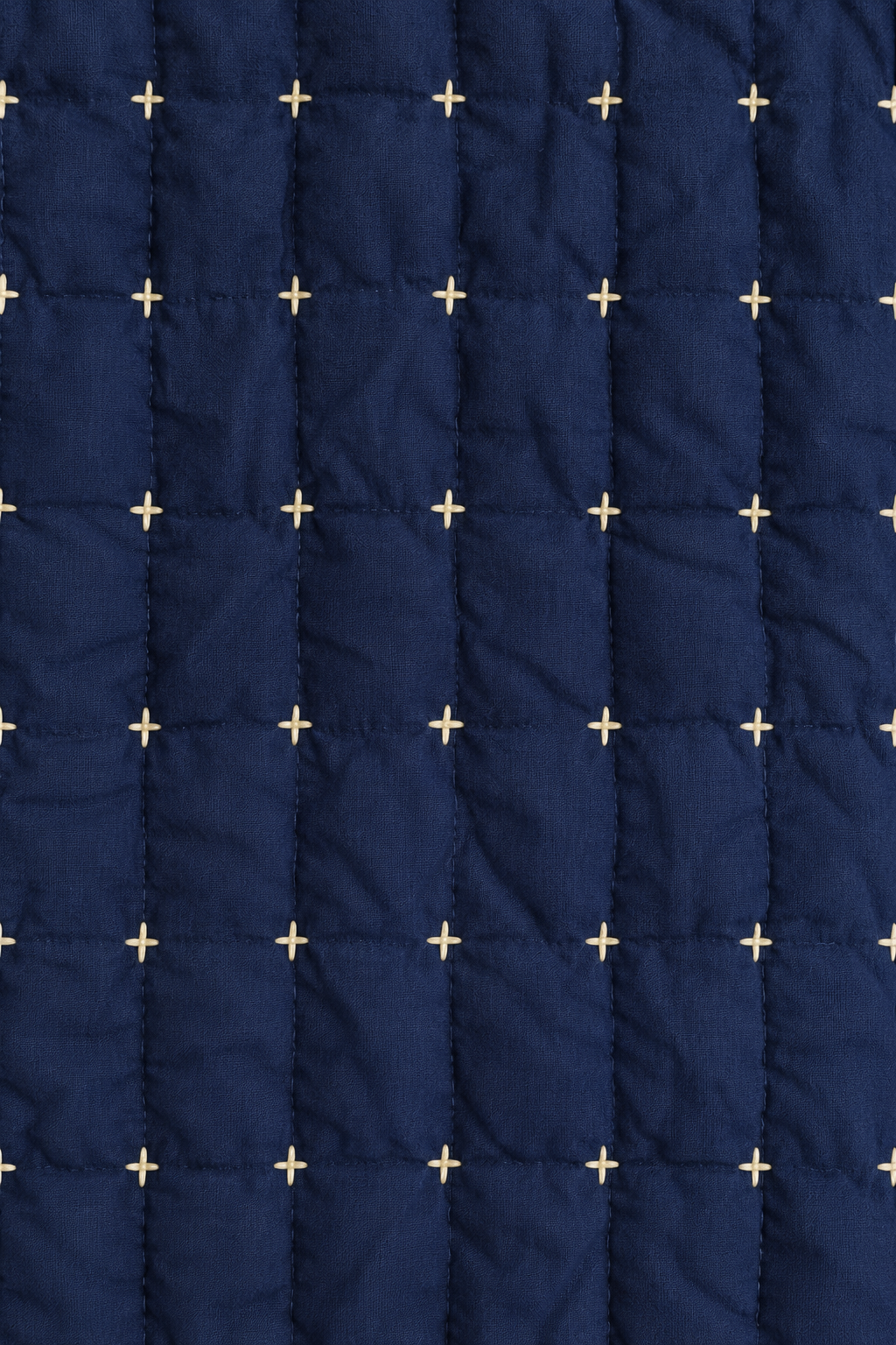 A close-up of a navy blue quilted fabric with a grid pattern and small cream embroidered plus-sign motifs.