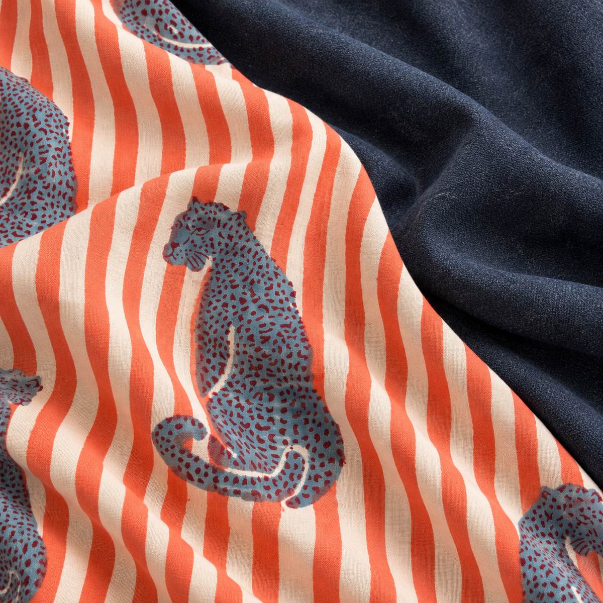 A close-up of draped fabric showing two different textures and patterns: one side features a navy blue plush fleece, and the other side shows a cream and orange striped fabric with blue leopard prints.